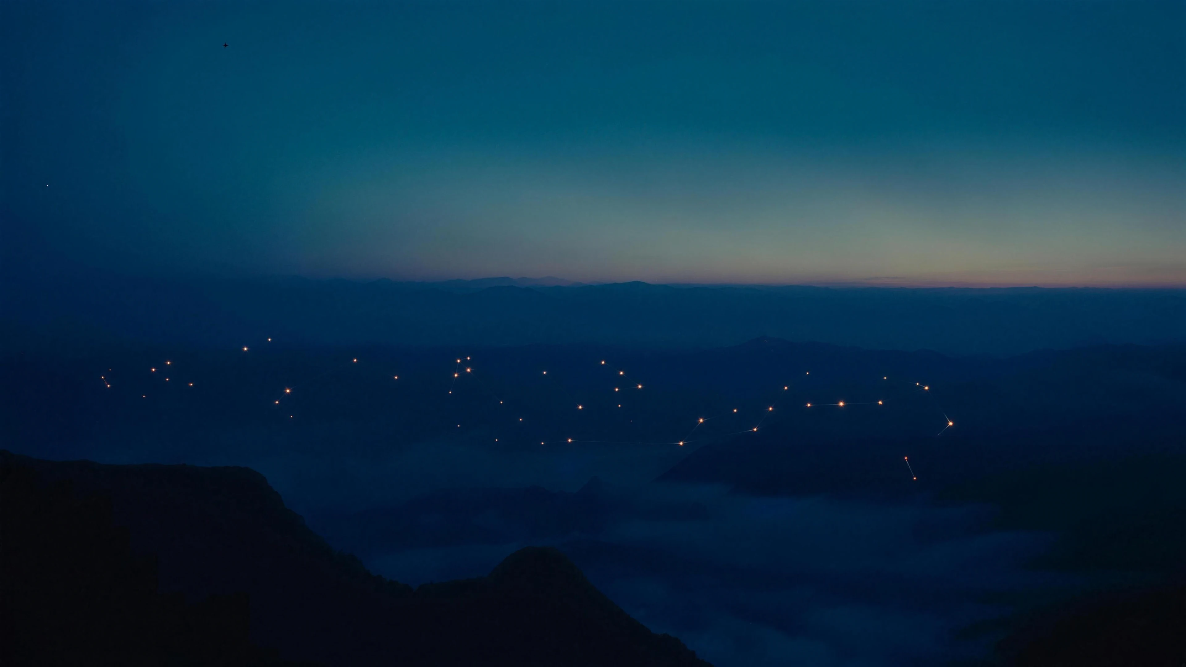 A valley at blue hour seen from a high ridge, small warm lights scattered across the far hills